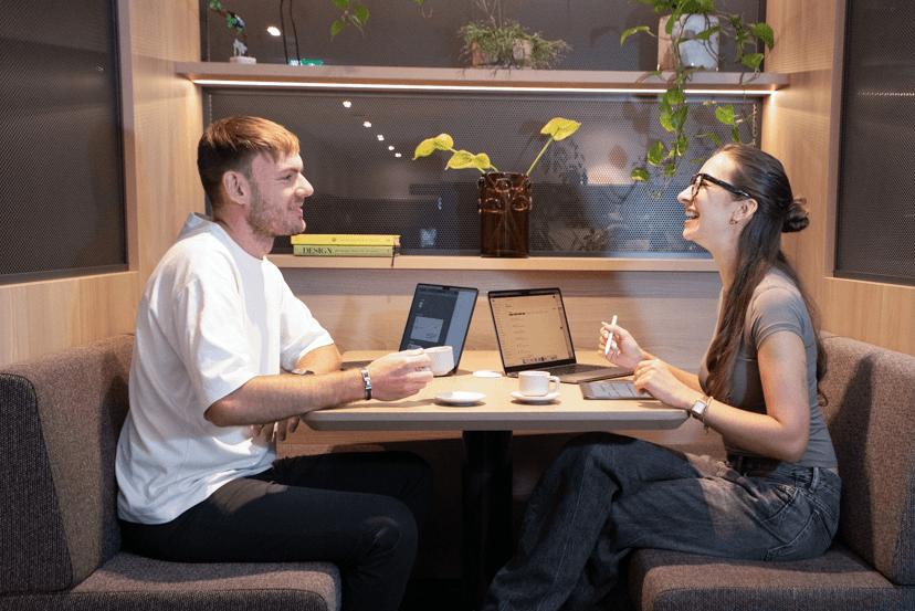 Lena und Ben am Tisch mit MacBooks und Kaffee